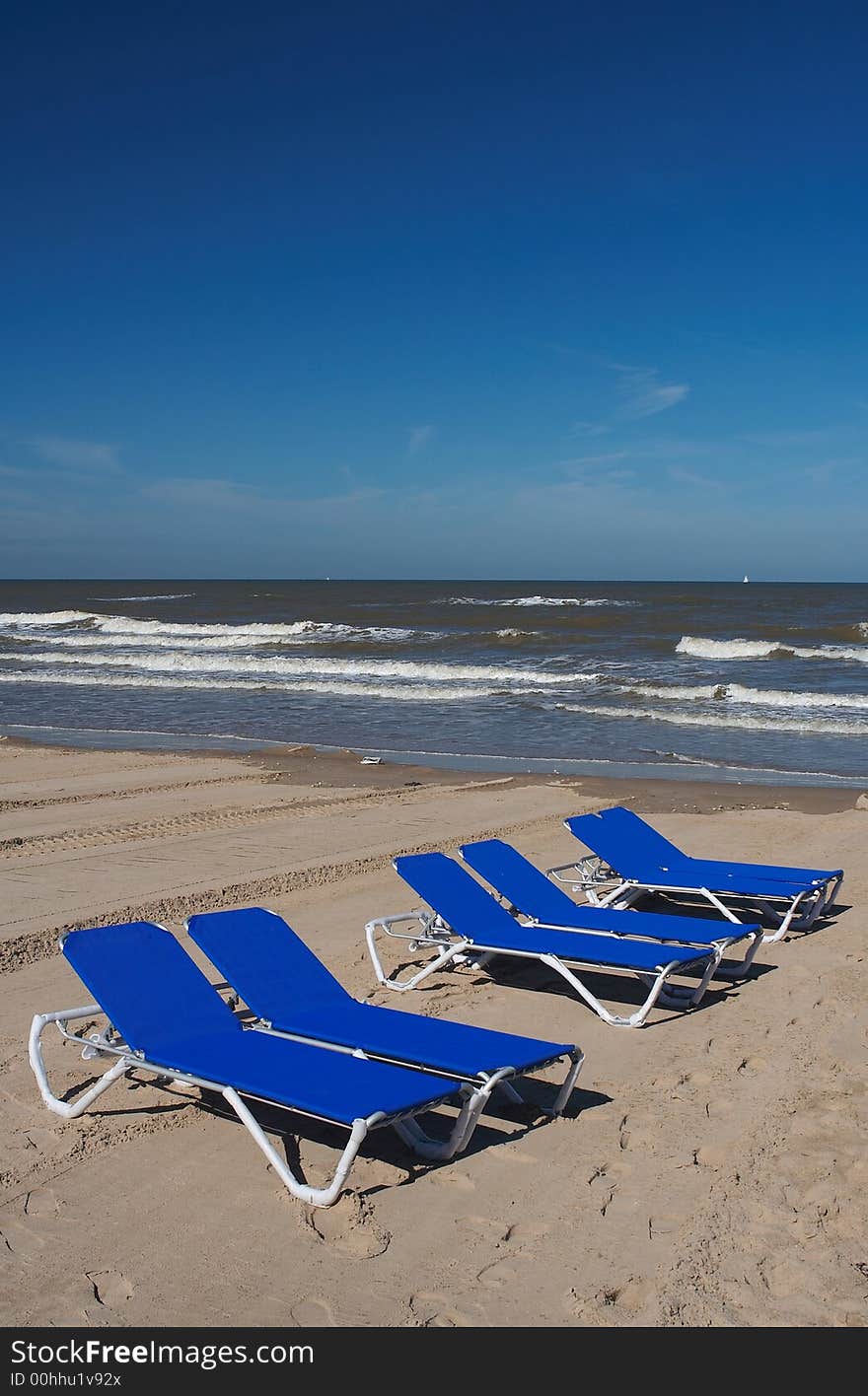 Six blue beach chairs in the sand with the sea/ocean on the background, plenty of copyspace. Six blue beach chairs in the sand with the sea/ocean on the background, plenty of copyspace