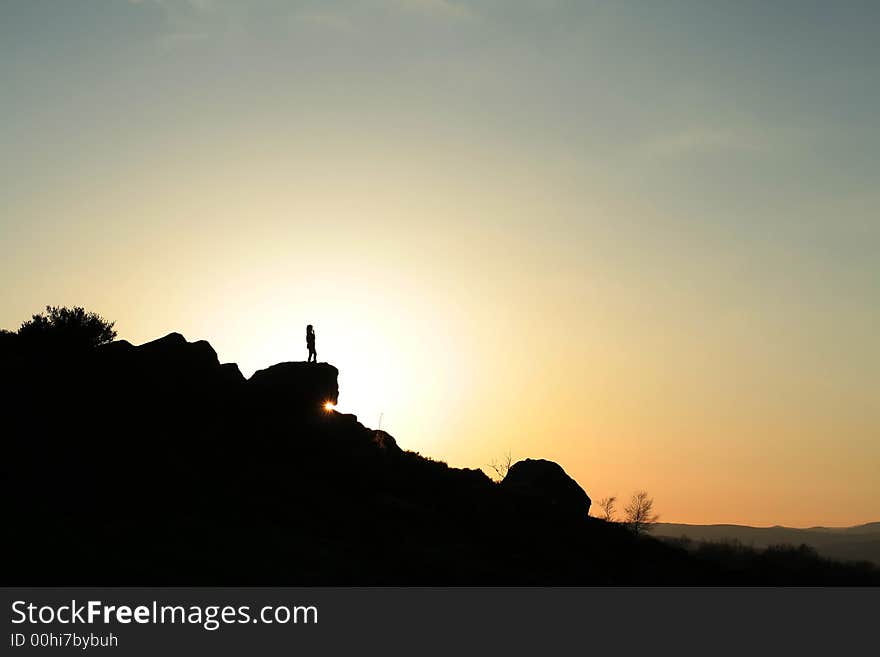 Girl silhouetted against the setting sun,stood on rock outcrop