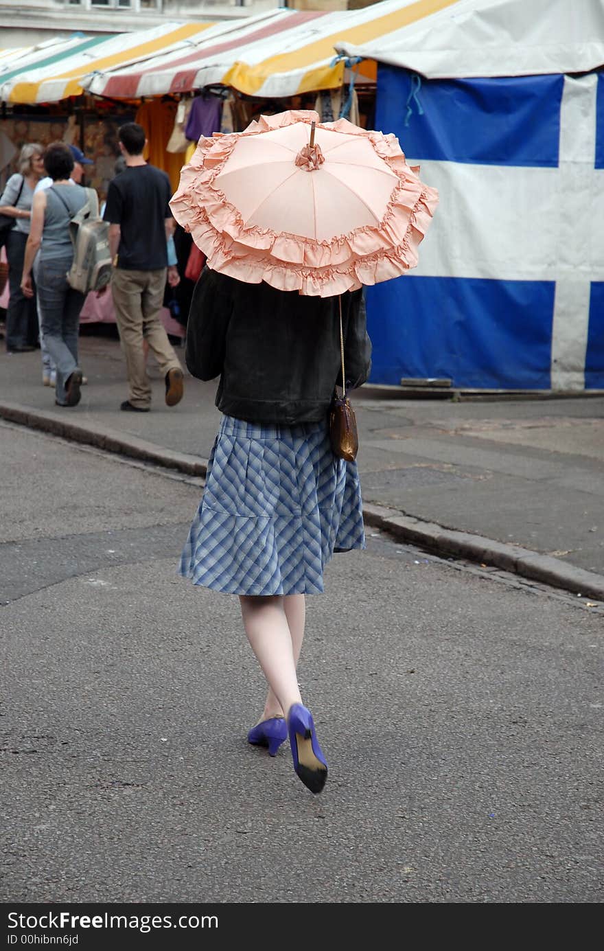 Woman walks through market shaded by pink parasol. Woman walks through market shaded by pink parasol.