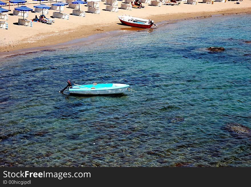 Small sandy beach, little harbour with motorboats, beach chairs and umbrella. Sunny day. Rhodes, Greece. Small sandy beach, little harbour with motorboats, beach chairs and umbrella. Sunny day. Rhodes, Greece.