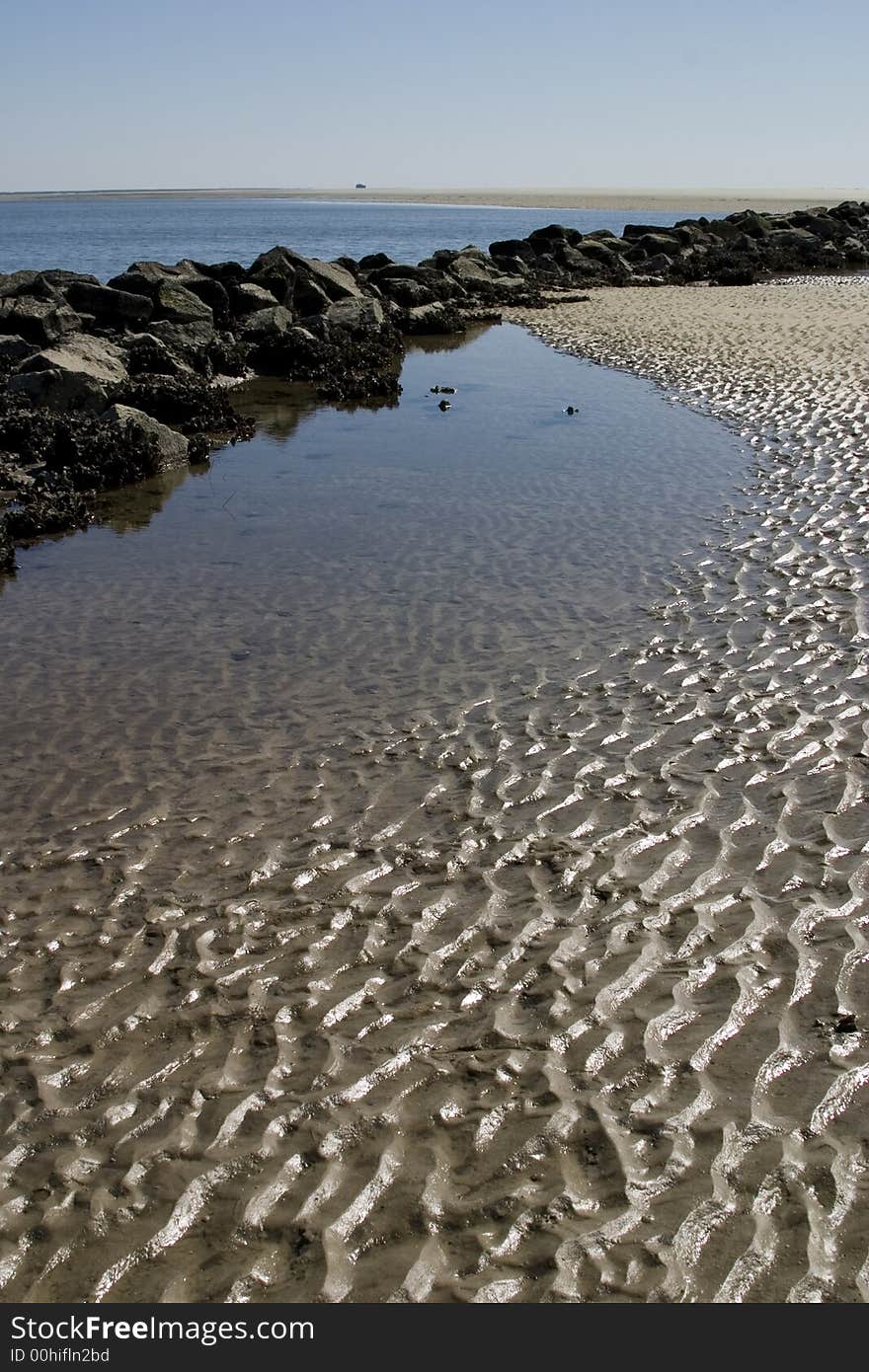 Sun lit ripples in the sand behind a jetty