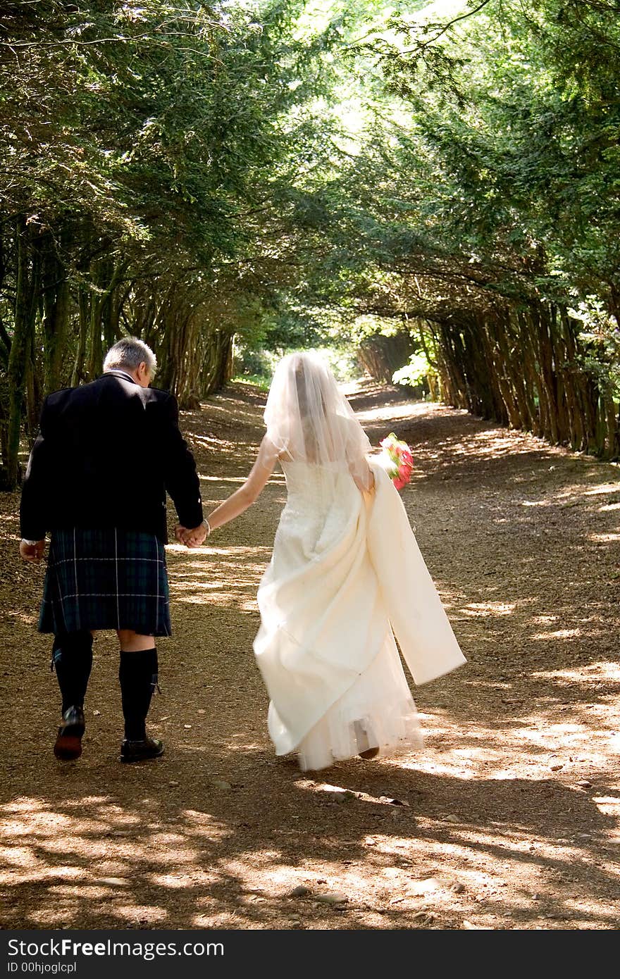 A bride & groom walking through a tree-lined avenue. A bride & groom walking through a tree-lined avenue