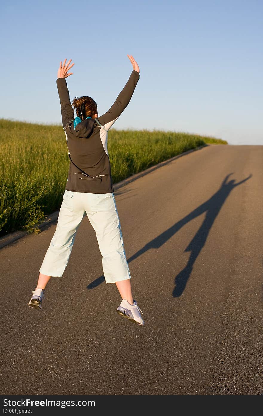 Woman from behind in sporty clothes. Cuts a caper - jumps into the air. Picture from behind with long shadow on the street.