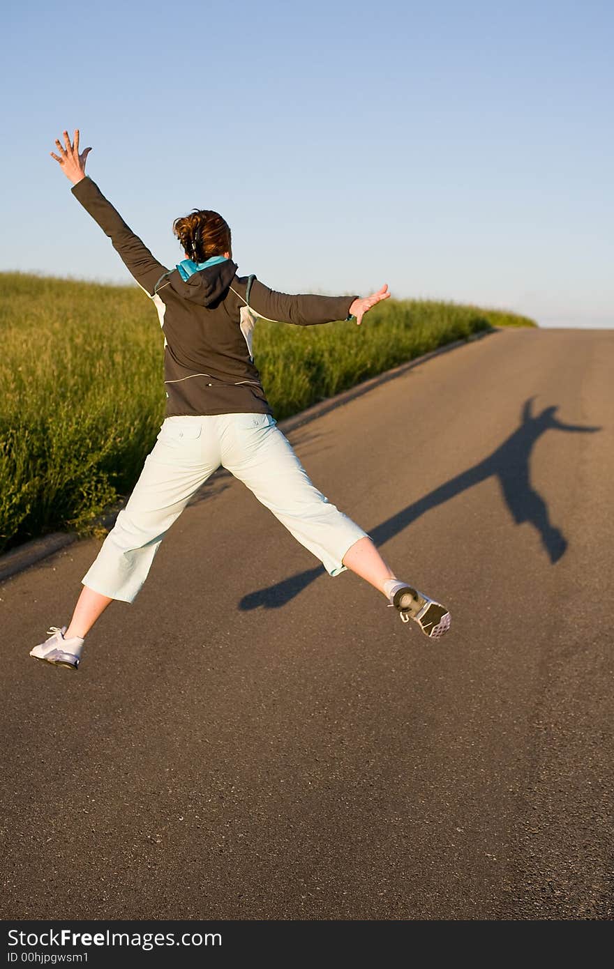 Woman from behind in sporty clothes. Cuts a caper - jumps into the air. Picture from behind with long shadow on the street. Woman from behind in sporty clothes. Cuts a caper - jumps into the air. Picture from behind with long shadow on the street.