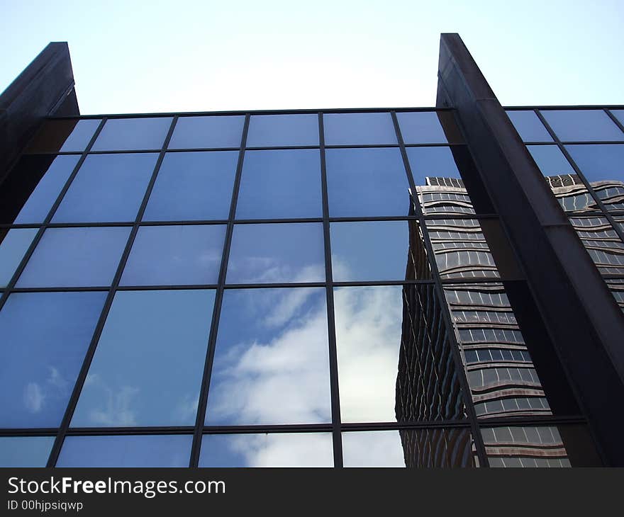 Clouds and an office building reflected in the mirrored windows of another office building with a pale blue sky above. Clouds and an office building reflected in the mirrored windows of another office building with a pale blue sky above.