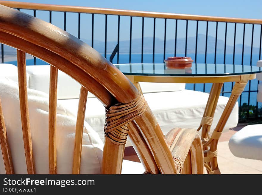 Back of chair and glass table in the bar of a luxury hotel, bright sun, see view in background. Back of chair and glass table in the bar of a luxury hotel, bright sun, see view in background