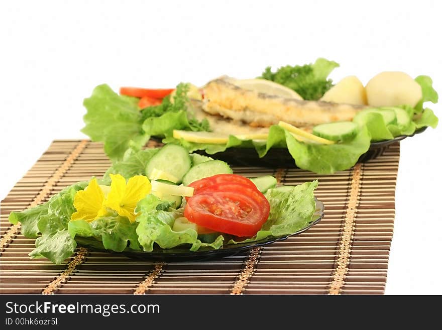 A plate with salad, on a background a dish with fried fish. A plate with salad, on a background a dish with fried fish.