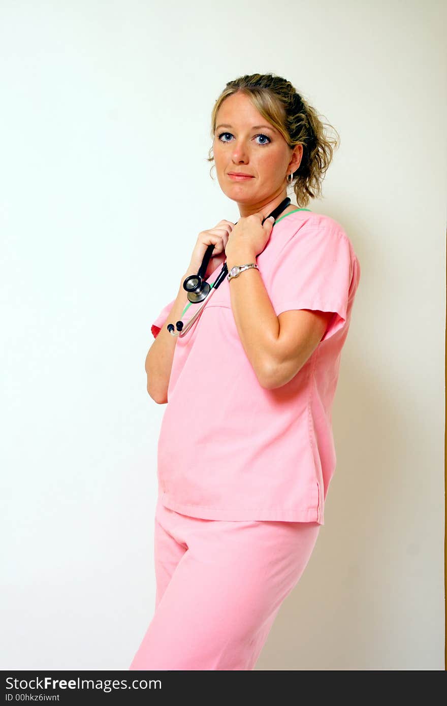 A nurse in pink scrubs holds on to her stethescope. A nurse in pink scrubs holds on to her stethescope.