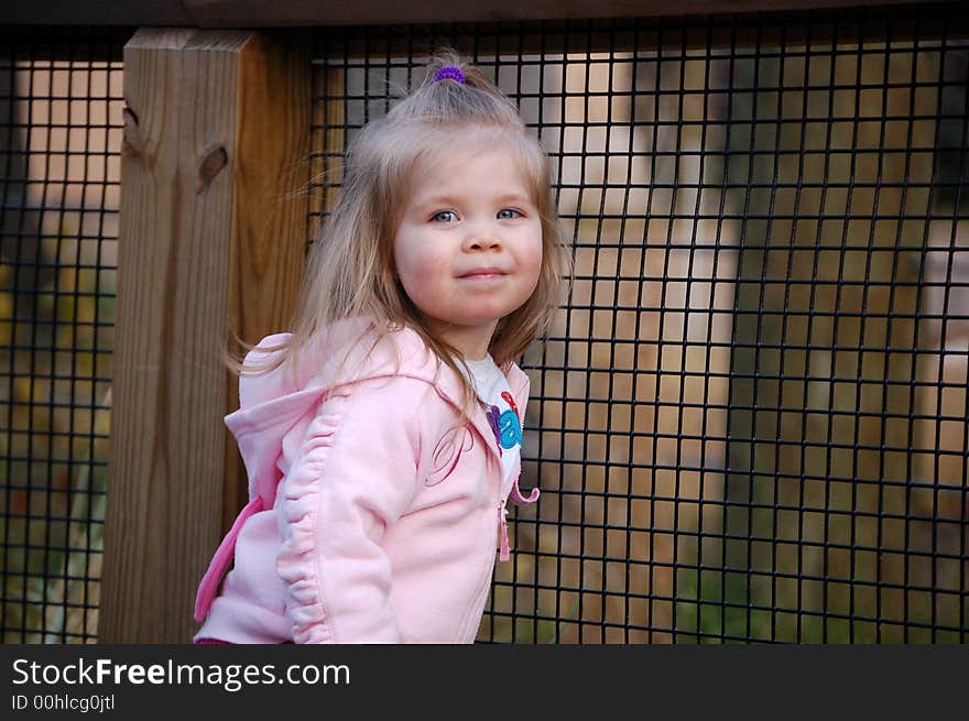 Two year old girl peeking through a fence. Two year old girl peeking through a fence.