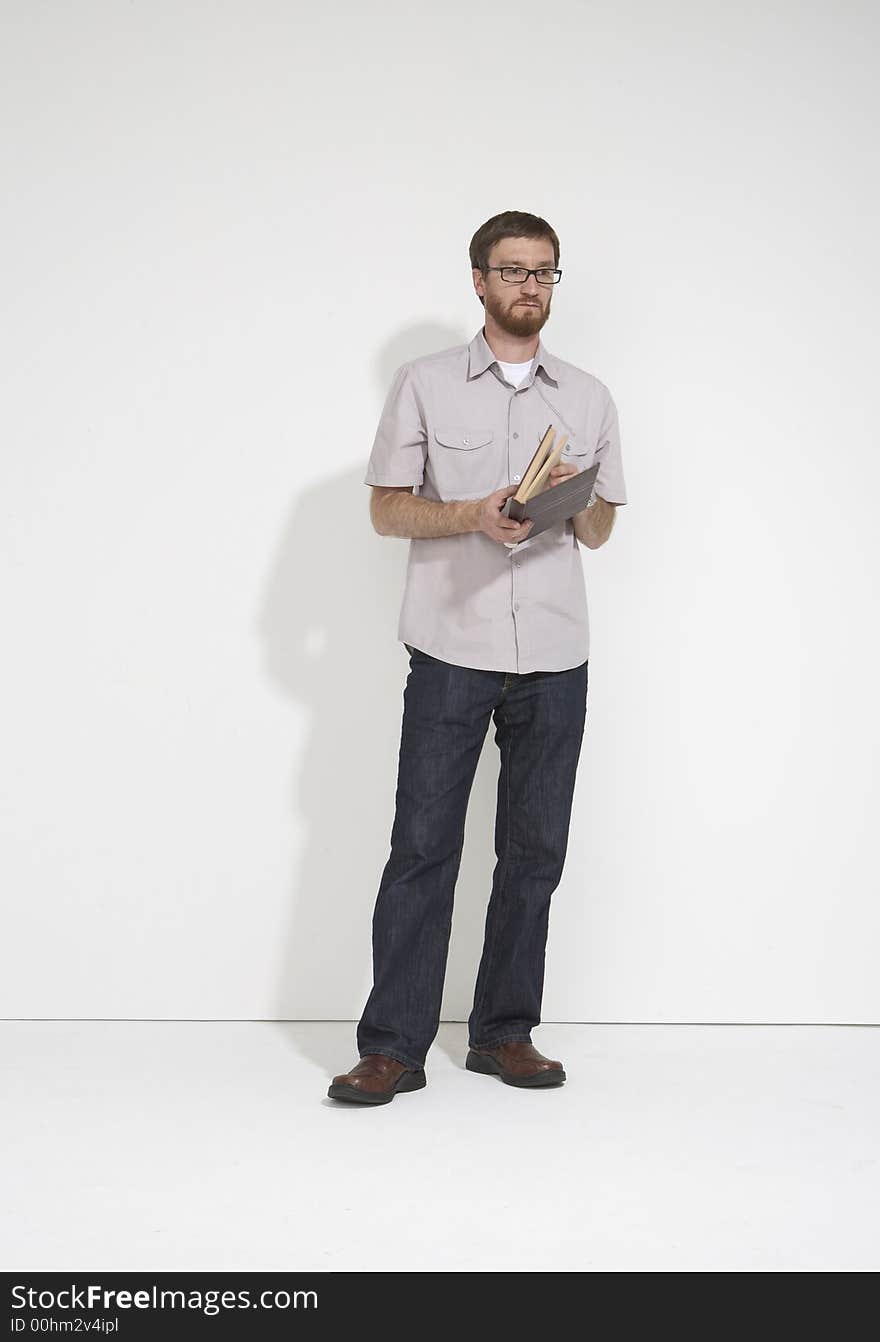 Man in a gray shirt and denim holding a brown book standing full length against a white studio wall. Man in a gray shirt and denim holding a brown book standing full length against a white studio wall.