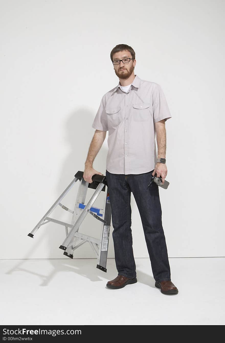 Man in a gray shirt and denim holding ladder about to speak standing full length against a white studio wall. Man in a gray shirt and denim holding ladder about to speak standing full length against a white studio wall.