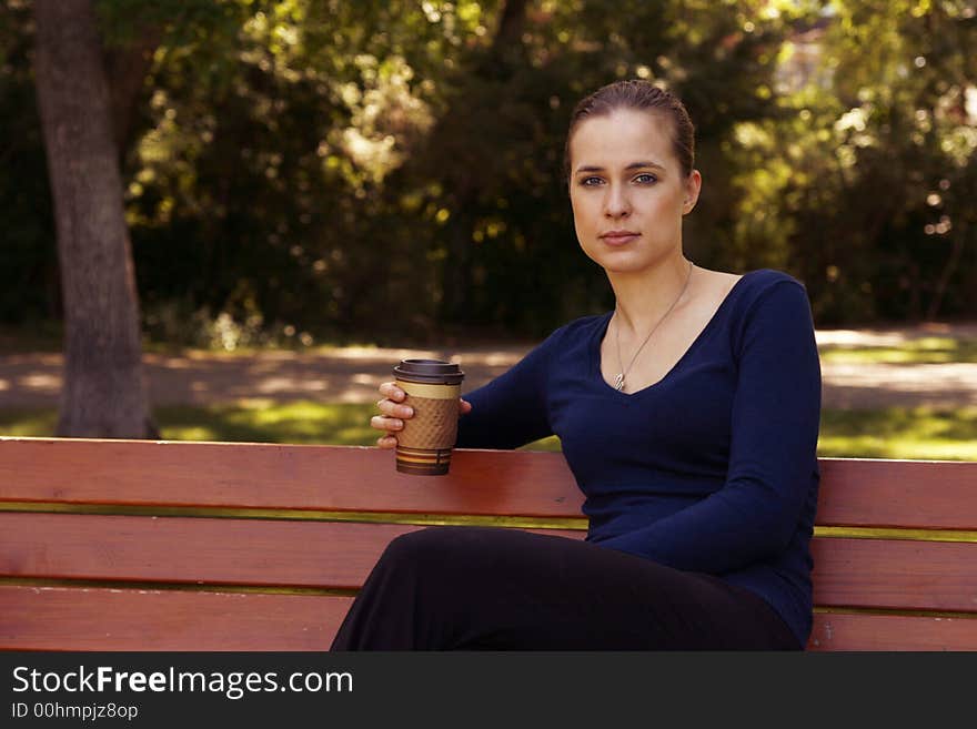 Woman sitting on a bench in a park during summer with a cup of coffee or tea in a cardboard cup. Woman sitting on a bench in a park during summer with a cup of coffee or tea in a cardboard cup.