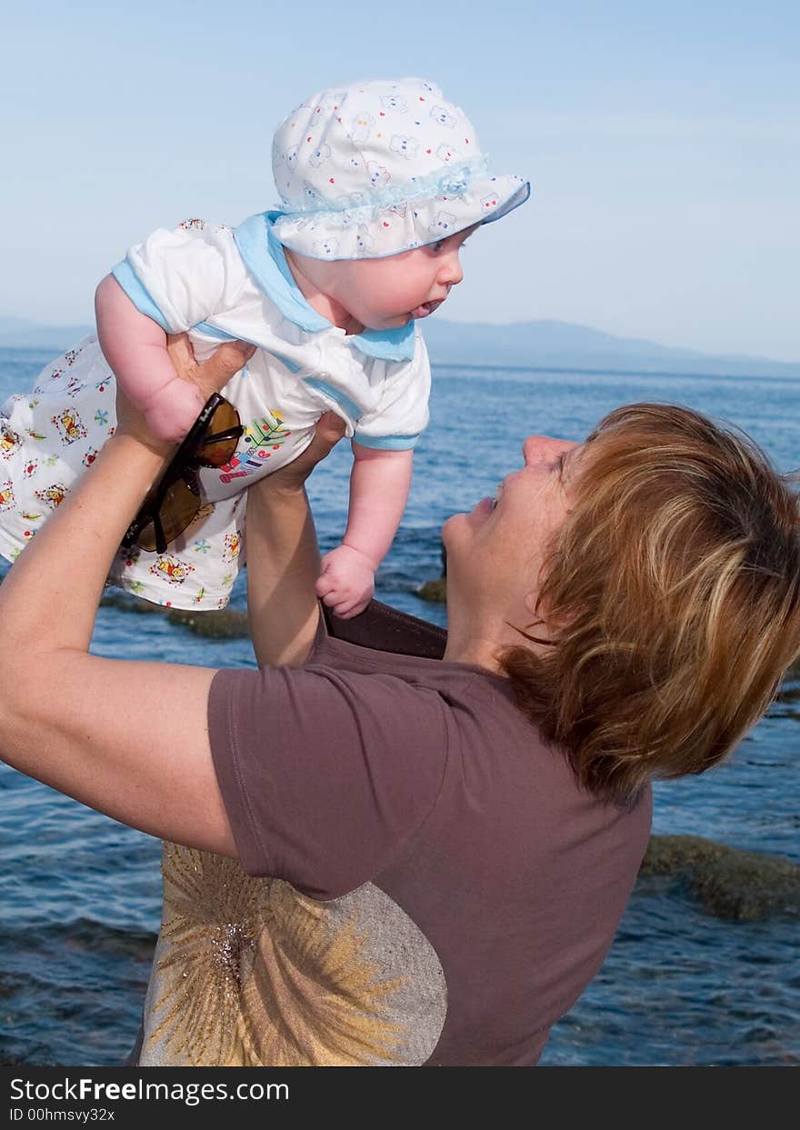 Family rest background representing mother holding her baby in the sky against sea landscape