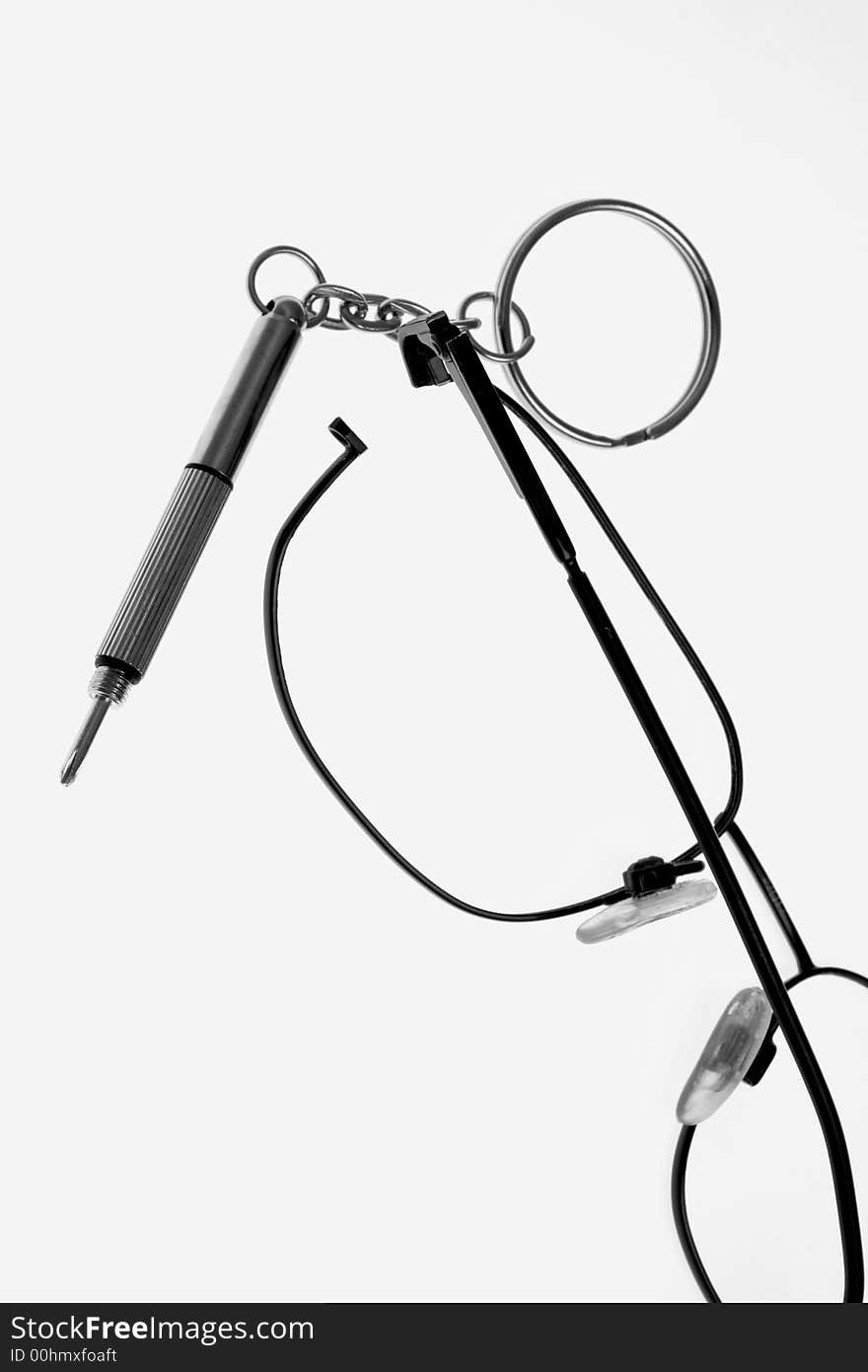 Broken eyeglasses with a Phillips head driver on white background.