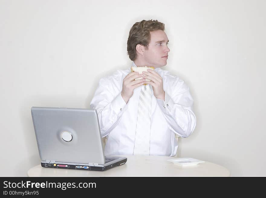 Businessman eating his sandwich and working on his laptop in his office. Businessman eating his sandwich and working on his laptop in his office