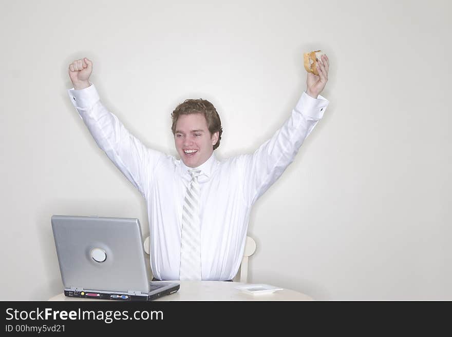 Businessman sitting at his table with his laptop and hands outstretched and in the air for success while holding his sandwich. Businessman sitting at his table with his laptop and hands outstretched and in the air for success while holding his sandwich