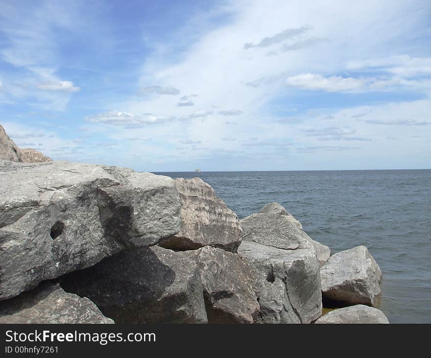 Huge rocks on the coast with water, and a cloudy blue sky. Huge rocks on the coast with water, and a cloudy blue sky.