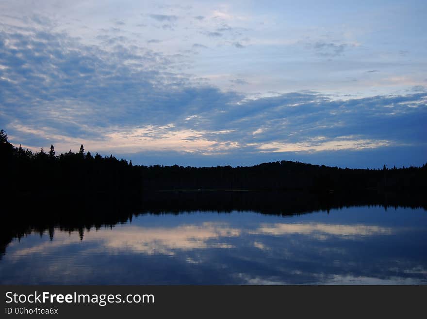 Cloud and sky reflected in lake with silhouetted shoreline. Cloud and sky reflected in lake with silhouetted shoreline