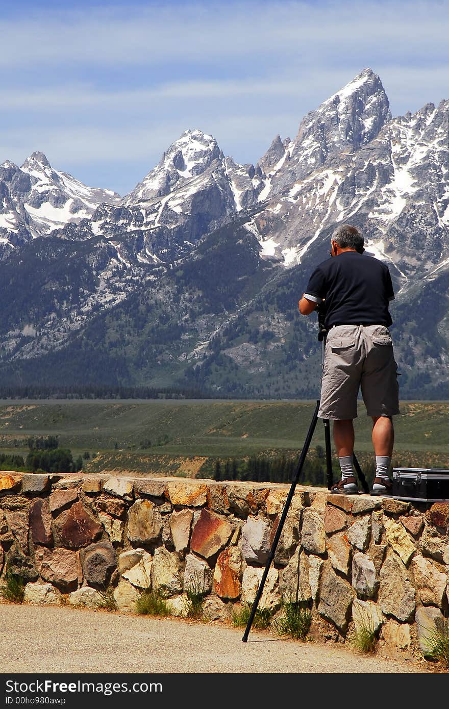 A photographer standing on a wall high above a valley to get his shot. Mountains in the background. A photographer standing on a wall high above a valley to get his shot. Mountains in the background.