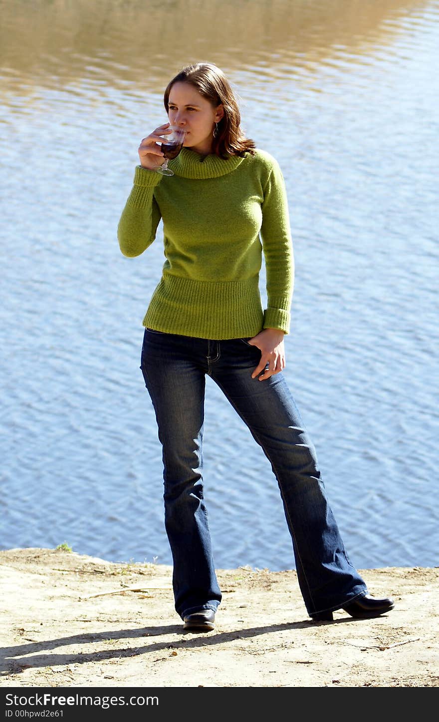 Young woman standing next to a river, enjoying a glass of wine. Young woman standing next to a river, enjoying a glass of wine.