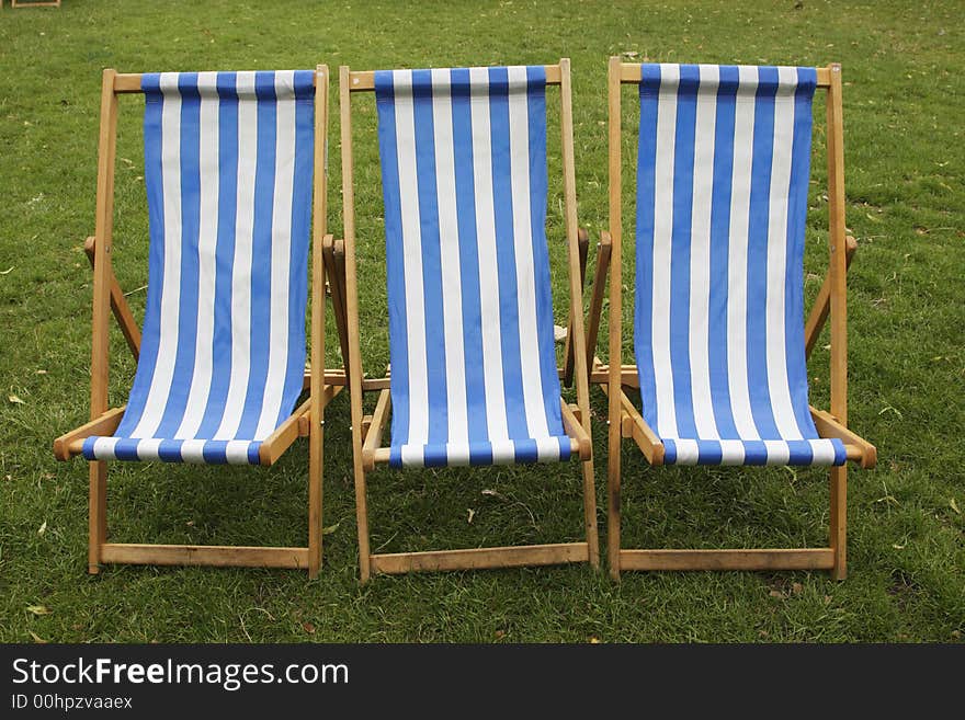 Three blue and white stripped empty deckchairs in a park london england uk taken in july 2007. Three blue and white stripped empty deckchairs in a park london england uk taken in july 2007