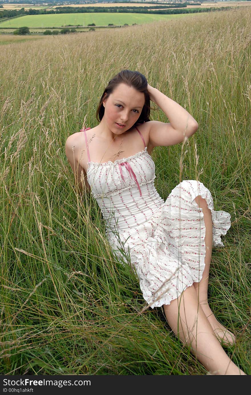 An attractive young brunette sits in the long grass on a summers day. An attractive young brunette sits in the long grass on a summers day.