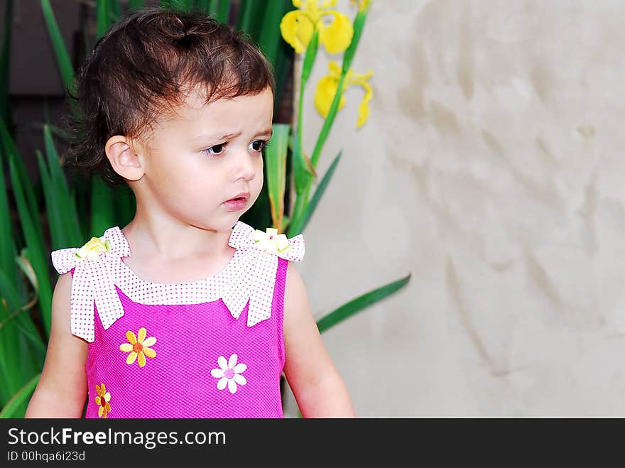 Cute child looking at something of interest.  She's outdoors dressed in a hot pink dress with greenery and yellow iris in the background. Cute child looking at something of interest.  She's outdoors dressed in a hot pink dress with greenery and yellow iris in the background.