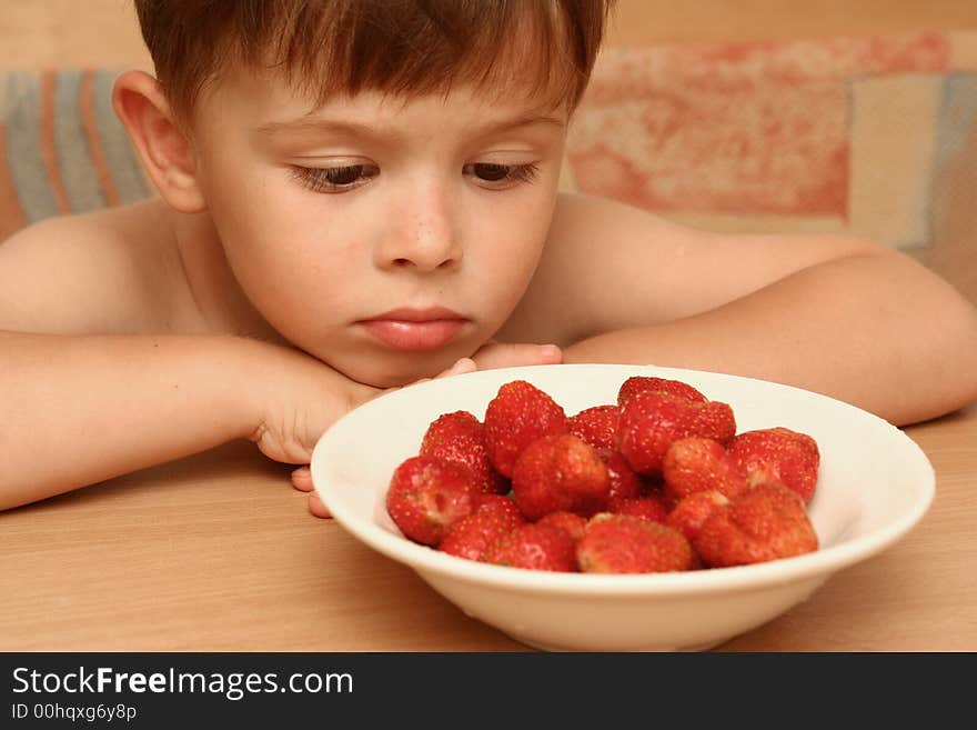 The child looks at a plate with red berries