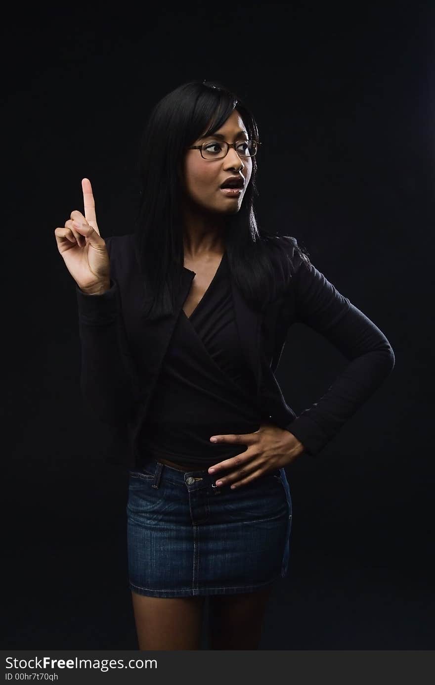 African America woman wearing glasses, black jacket and top with a denim mini skirt. She has her right hand and indew finger pointed to sky and a surprised expression on her face. African America woman wearing glasses, black jacket and top with a denim mini skirt. She has her right hand and indew finger pointed to sky and a surprised expression on her face.