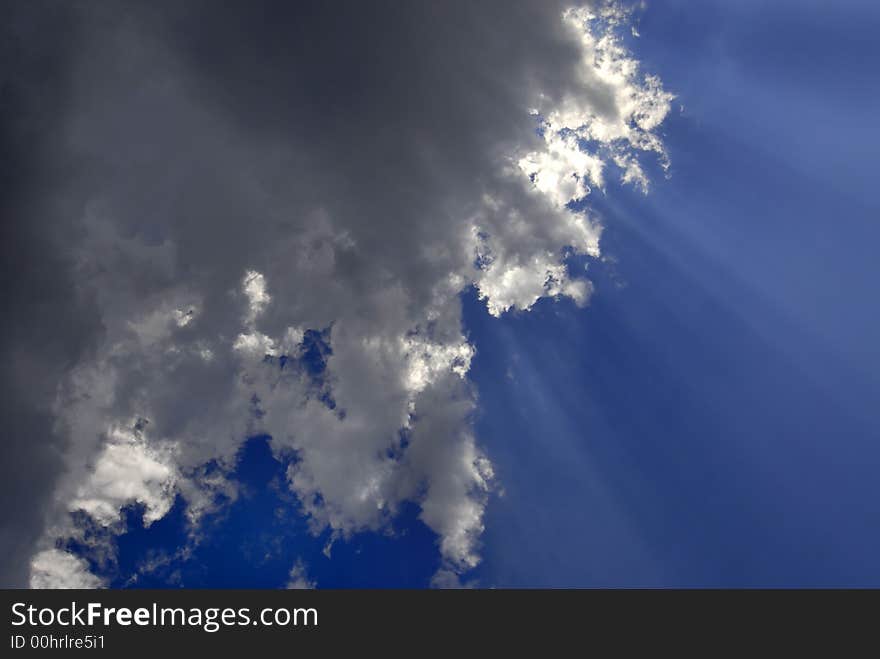 View of white and gray storm clouds in blue sky with rays of light. View of white and gray storm clouds in blue sky with rays of light