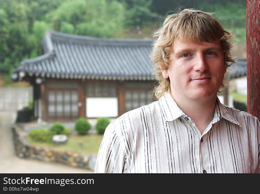 Blond man smiling with oriental buildings in the background - travel and tourism. NOTE: Light rain, not noise.