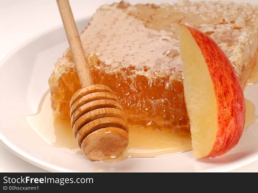 A honeycomb and honey wand on a white plate with an apple slice. A honeycomb and honey wand on a white plate with an apple slice