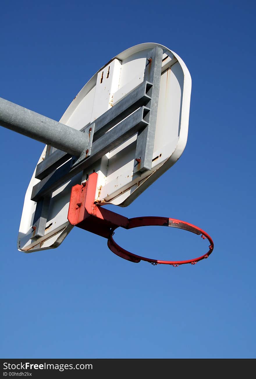 A playground basketball hoop against a blue sky.