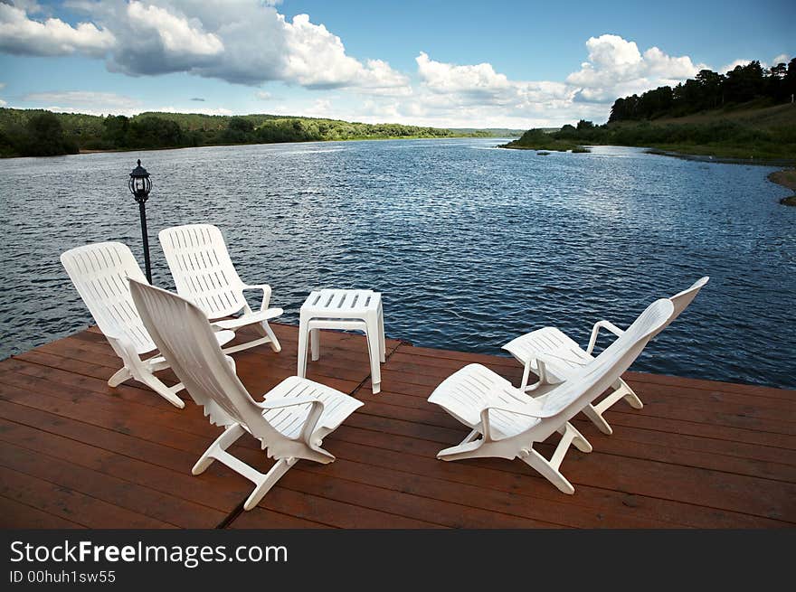 Five white armchairs and table on coast of a reservoir