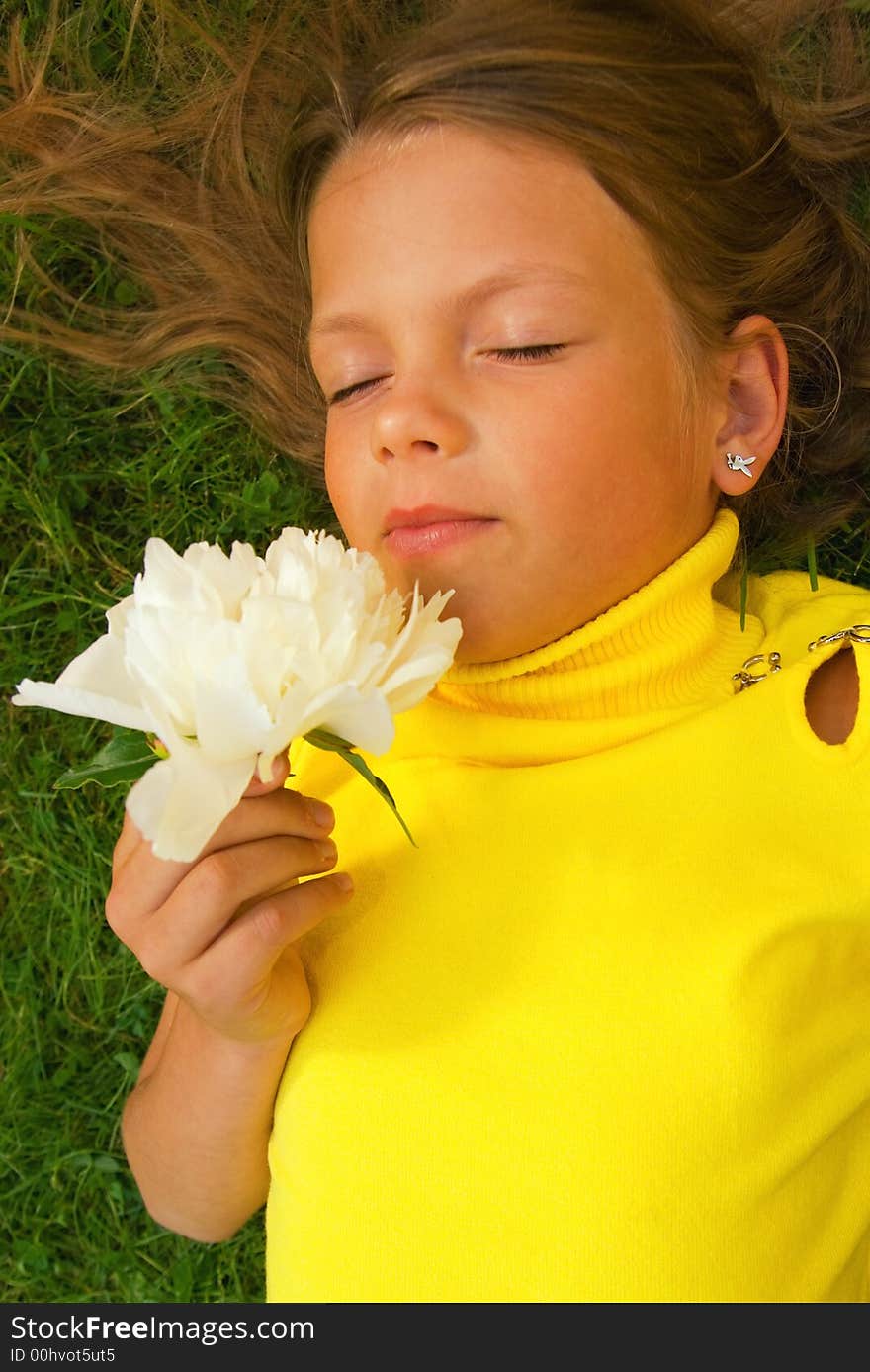 Little girl with a white flower lying on a green grass