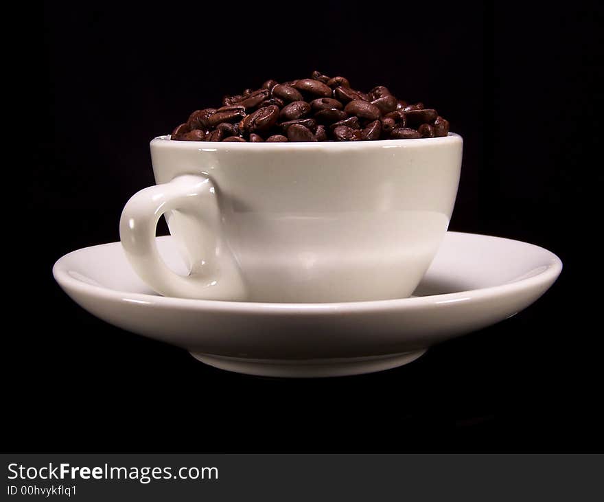 Simple white cup full of coffee beans sitting on a matching saucer on a black background. Simple white cup full of coffee beans sitting on a matching saucer on a black background.