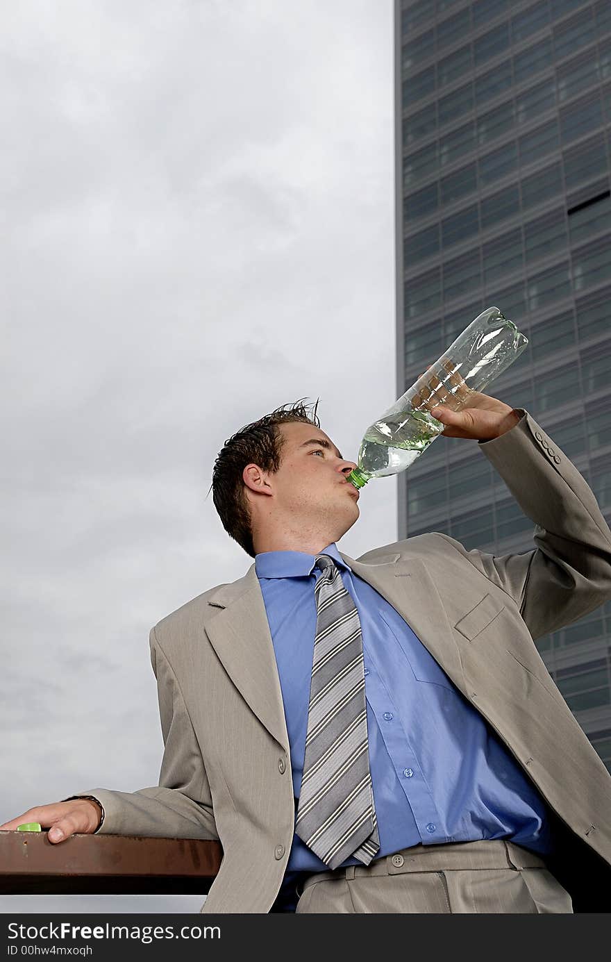 Businessman drinking water from plastic bottle in front of business building.