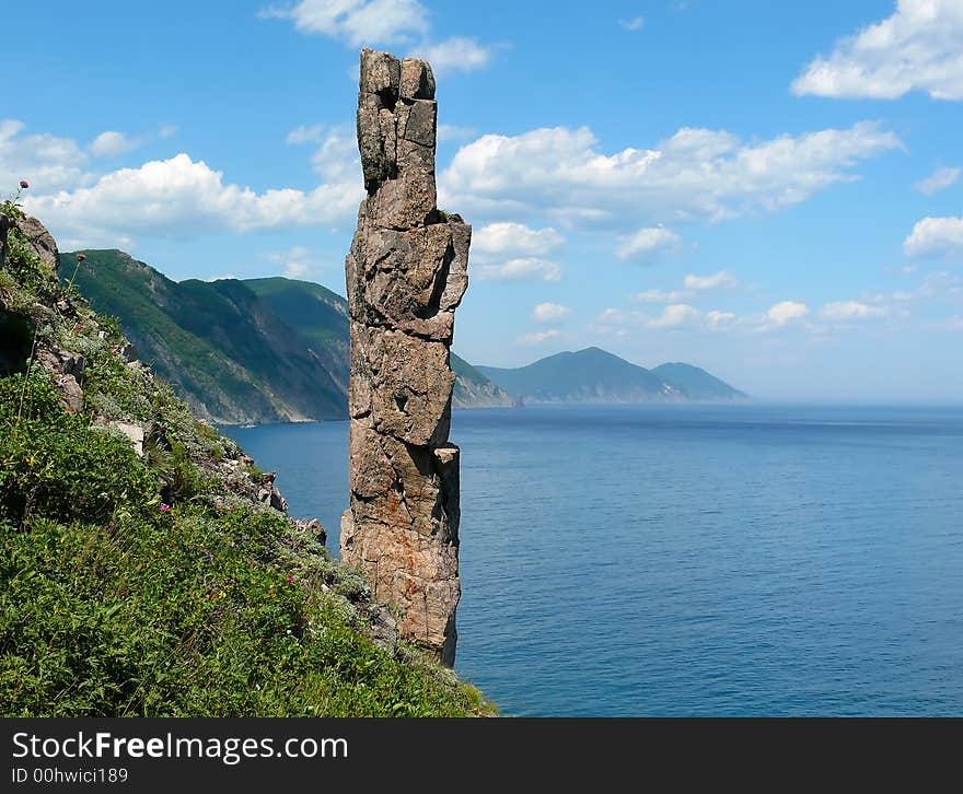 On foreground the single vertical rock with name Hare. On background turquoise sea, cliffs and sky with white clouds. Russian Far Easr, Primorye, Japanese sea, Tasovaya Bay. On foreground the single vertical rock with name Hare. On background turquoise sea, cliffs and sky with white clouds. Russian Far Easr, Primorye, Japanese sea, Tasovaya Bay.