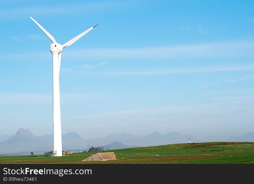 Wind powered electricity generator standing against the blue sky in a green field on the wind farm. Wind powered electricity generator standing against the blue sky in a green field on the wind farm