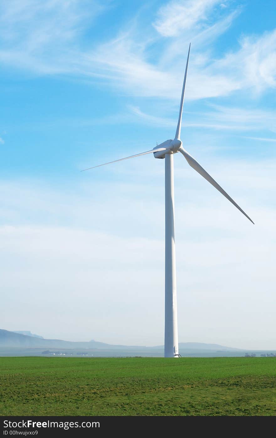 Wind powered electricity generator standing against the blue sky in a green field on the wind farm. Wind powered electricity generator standing against the blue sky in a green field on the wind farm