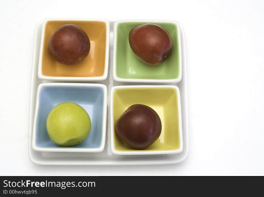 One yellow and three red plums on colorful plates. One yellow and three red plums on colorful plates.