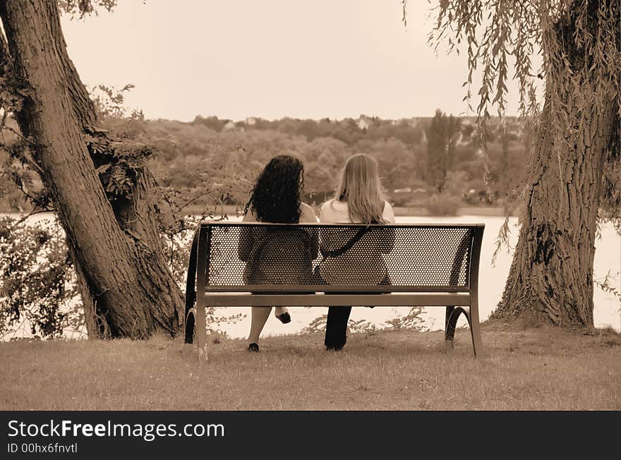 Two girls sitting on a bench in a park. Two girls sitting on a bench in a park