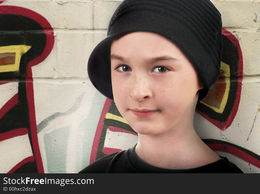 A kid in the street standing against a wall with graffiti and trying to look tough. A kid in the street standing against a wall with graffiti and trying to look tough