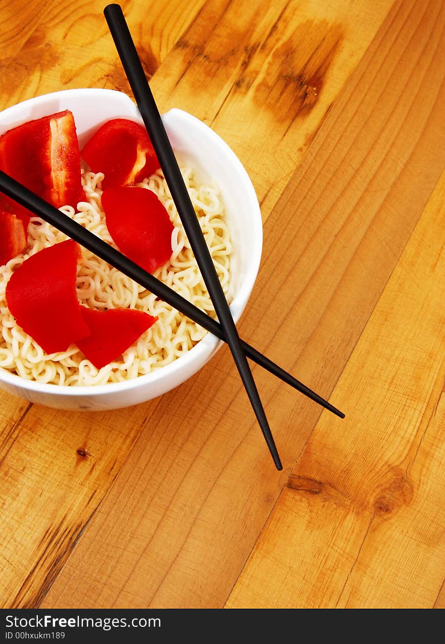 Chinece noodles with chop sticks in a bowl on wooden counter with some peppers in the noodles. Chinece noodles with chop sticks in a bowl on wooden counter with some peppers in the noodles