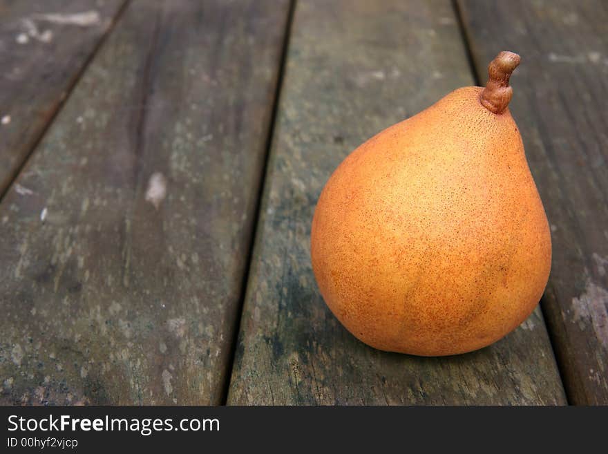 A yellow brown ripe pear on a weathered wooden park table