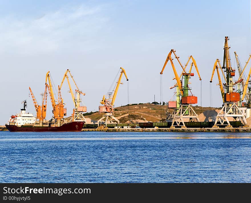 Seaport on a background of picturesque mountains. Elevating cranes with bright colors