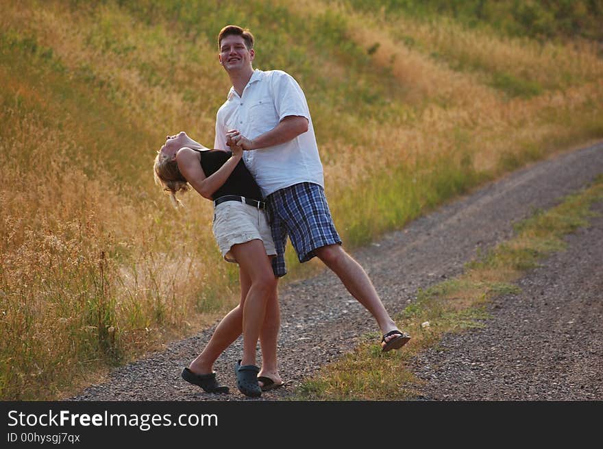 A young couple jokes around while walking down a dirt road in the countryside. A young couple jokes around while walking down a dirt road in the countryside.