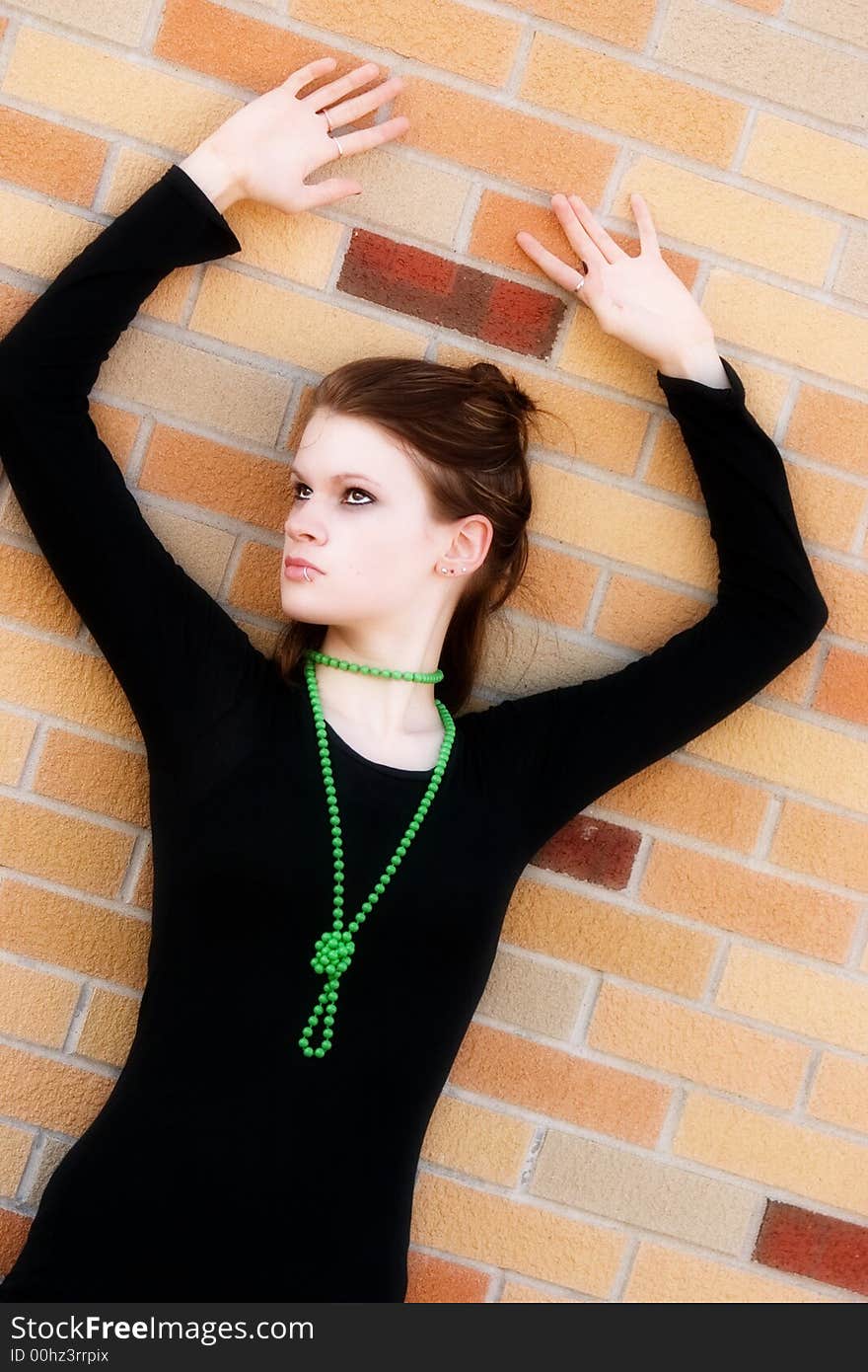 Serious teen in black pressed against a bright wall with her hands overhead. Serious teen in black pressed against a bright wall with her hands overhead.