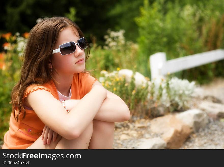 Portrait of an attractive preteen in a sunny garden gazing into the distance through her sunglasses. Portrait of an attractive preteen in a sunny garden gazing into the distance through her sunglasses.