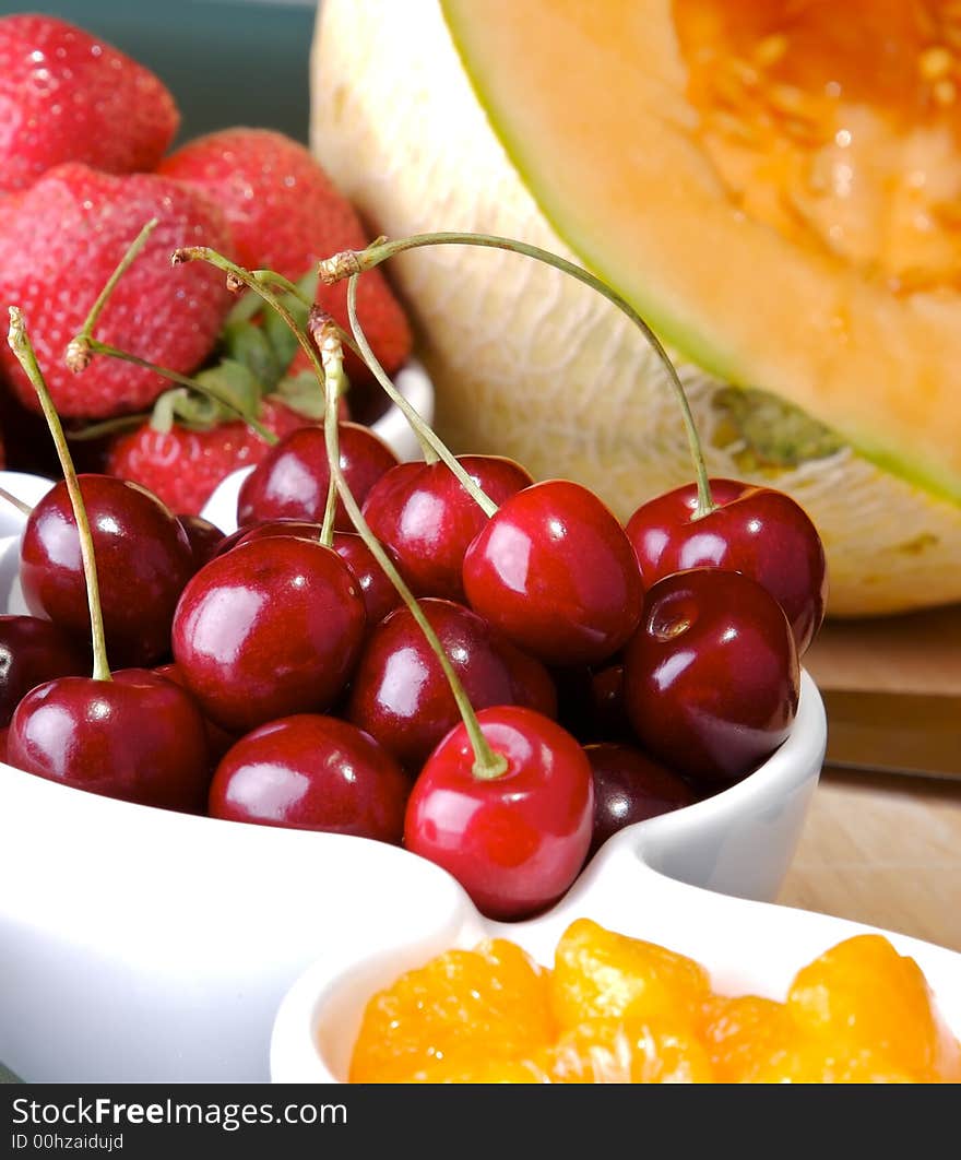 Small bowls of strawberries, cherries, and mandarin orange slices with a cantaloupe in the back. Small bowls of strawberries, cherries, and mandarin orange slices with a cantaloupe in the back.